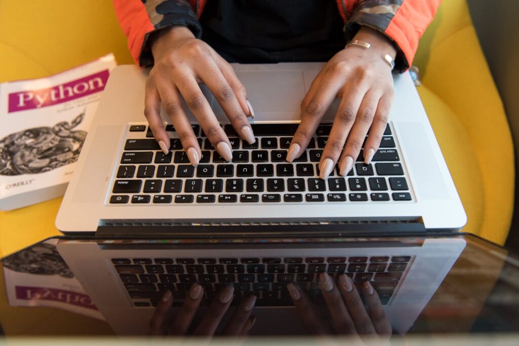 A person typing on a laptop with a Python programming book visible, capturing technology and learning.